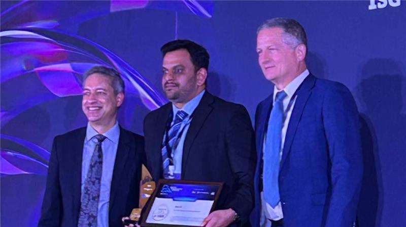 Three people standing on stage during an awards ceremony, with one person holding a trophy and a framed certificate.