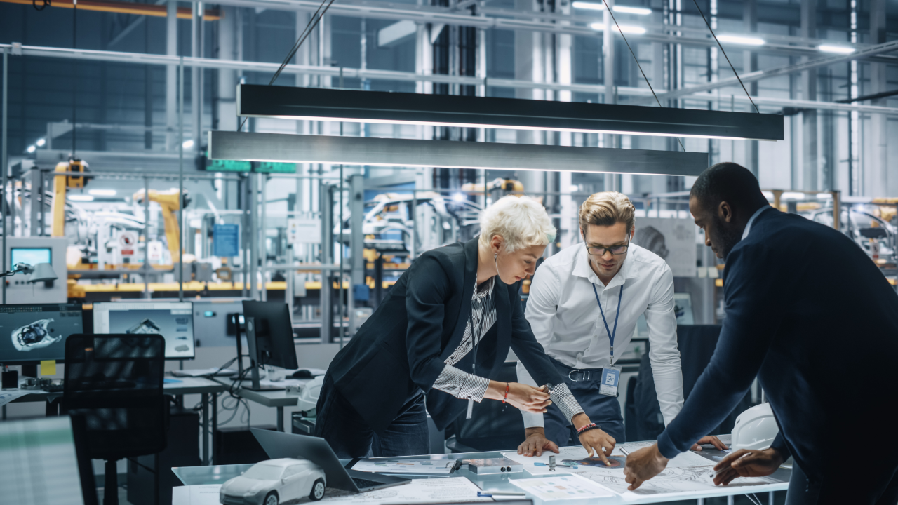one woman and two men working on a project an a table in an engineering factory