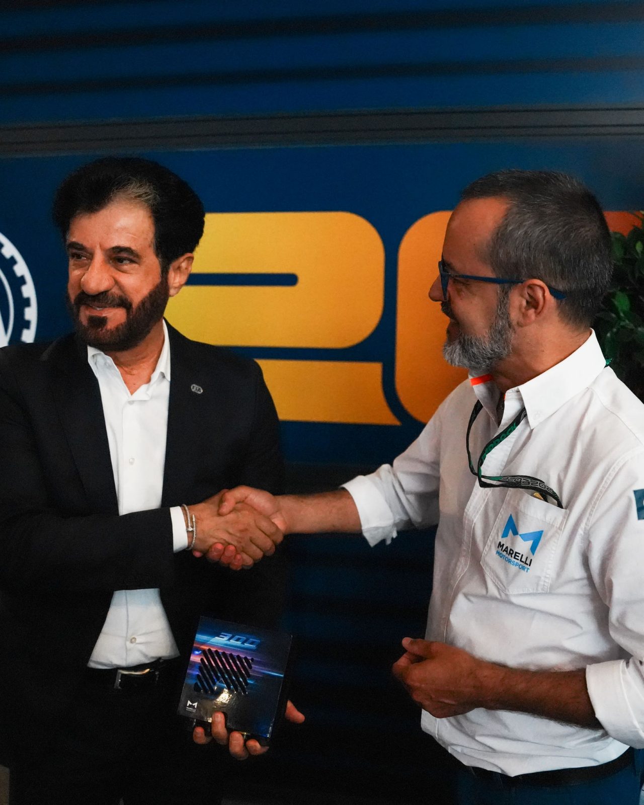 Due professionisti si stringono la mano mostrando un componente elettronico Marelli.