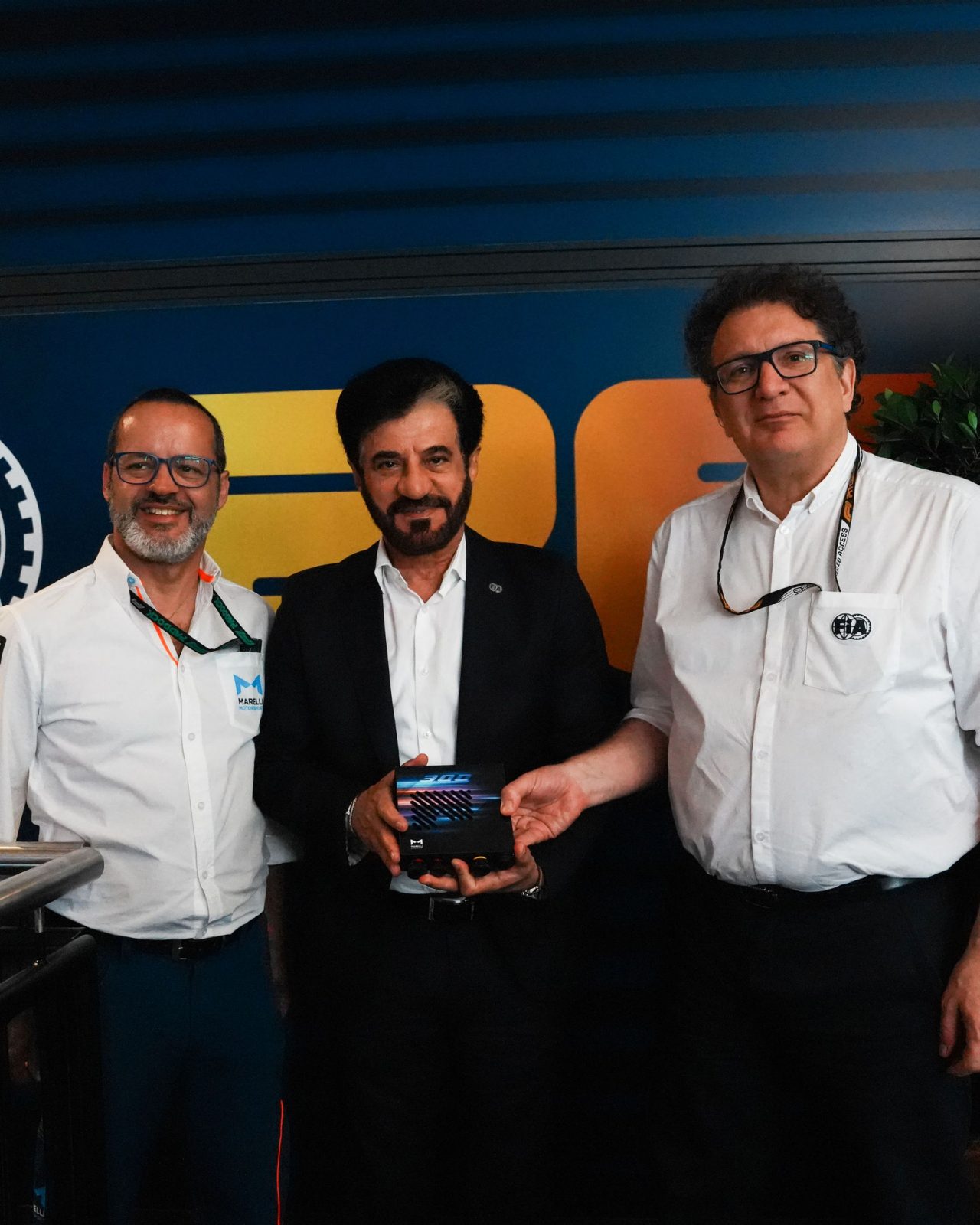 Tre professionisti presentano un dispositivo elettronico Marelli allo stand.