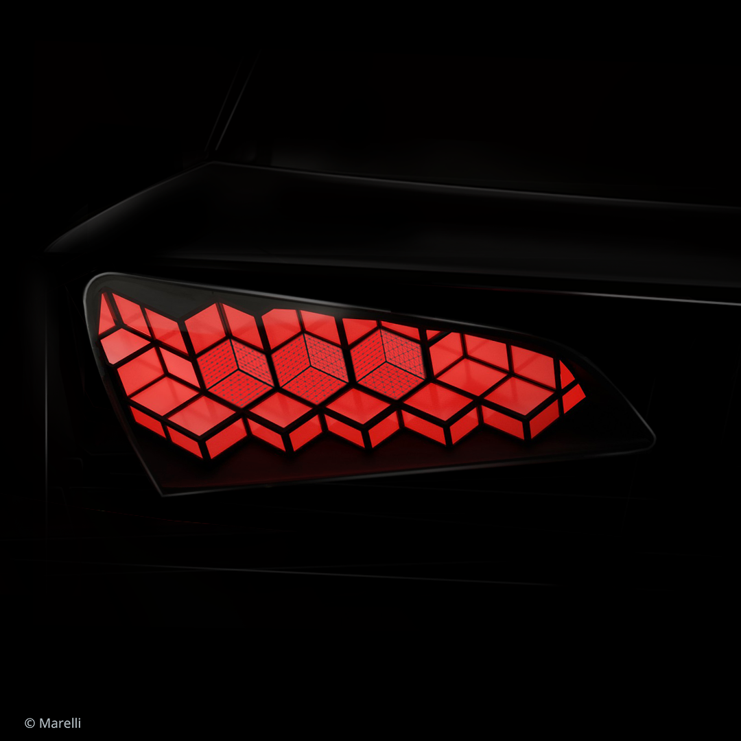 Close-up of a sleek car taillight glowing red, featuring a geometric honeycomb pattern set into a glossy black body panel against a dark background.